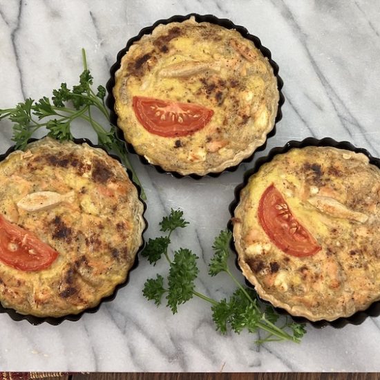 Three fish tarts with parsley on a marble counter.