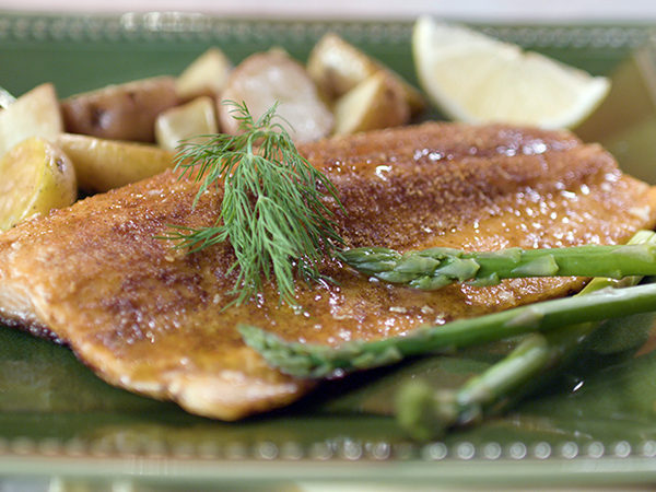 This is a photograph of seared fish accented by asparagus, lemon, potatoes and dill on a green plate.