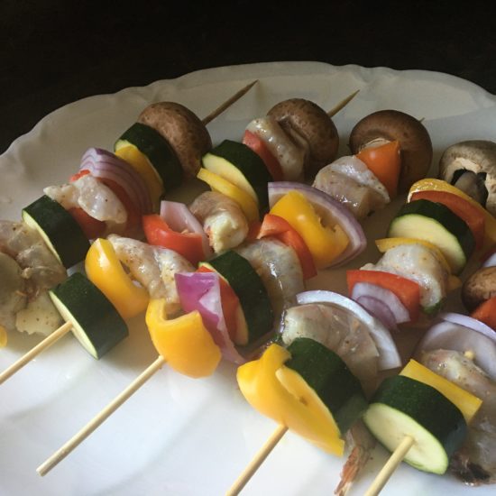 Grilled fish, pork, mushrooms, onions, pepper, and cucumber on a cabob.