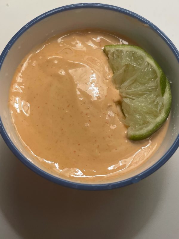 Salmon sashimi in citrus-ginger-sesame sause with a lime on top in a white and blue bowl.