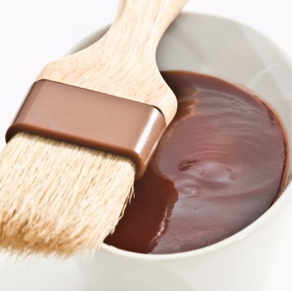 BBQ sauce in a small white dish with a dressing brush balanced on top.