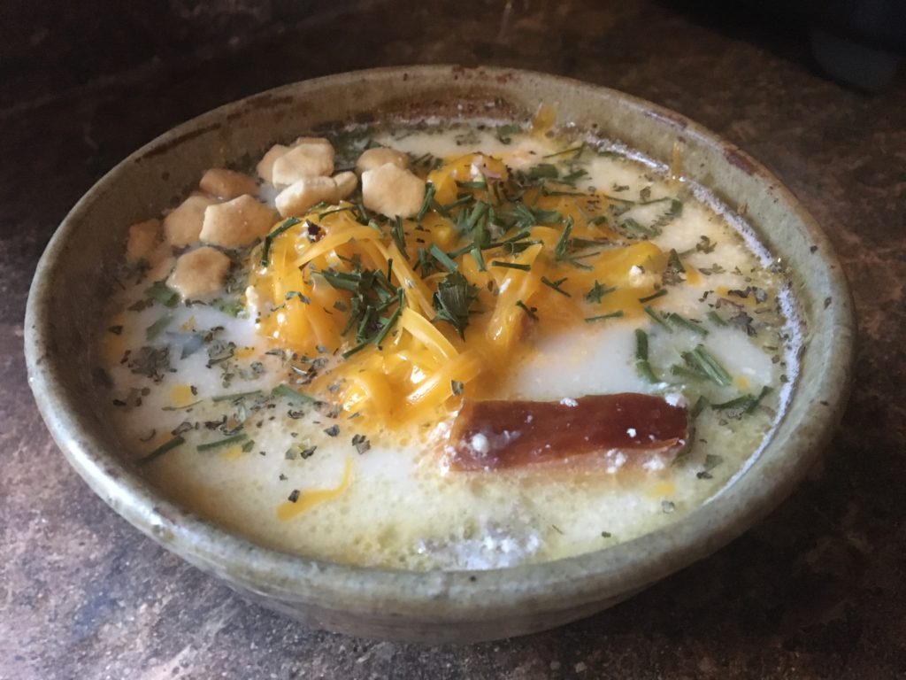 A bowl of fish chowder topped with cheese, oyster crackers and chives.