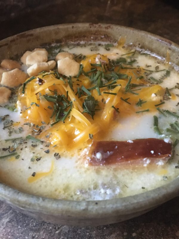 A bowl of fish chowder topped with cheese, oyster crackers and chives.