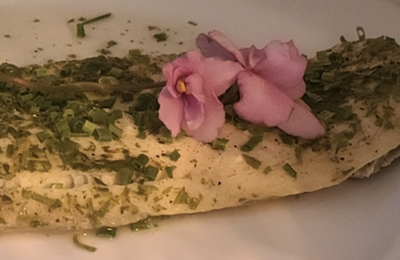Lake whitefish sprinkled with green onions and a bright pink flower